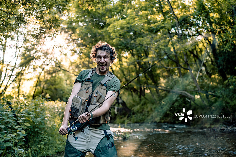 快乐的渔夫在宁静的森林溪流中享受钓鱼的一天图片素材