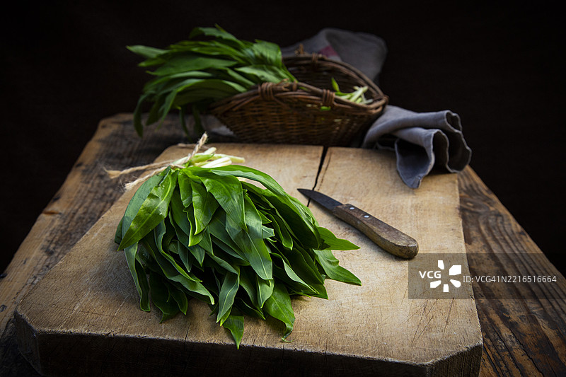 一束野蒜放在乡村风格的砧板上，旁边有一把刀和一个柳条篮子图片素材