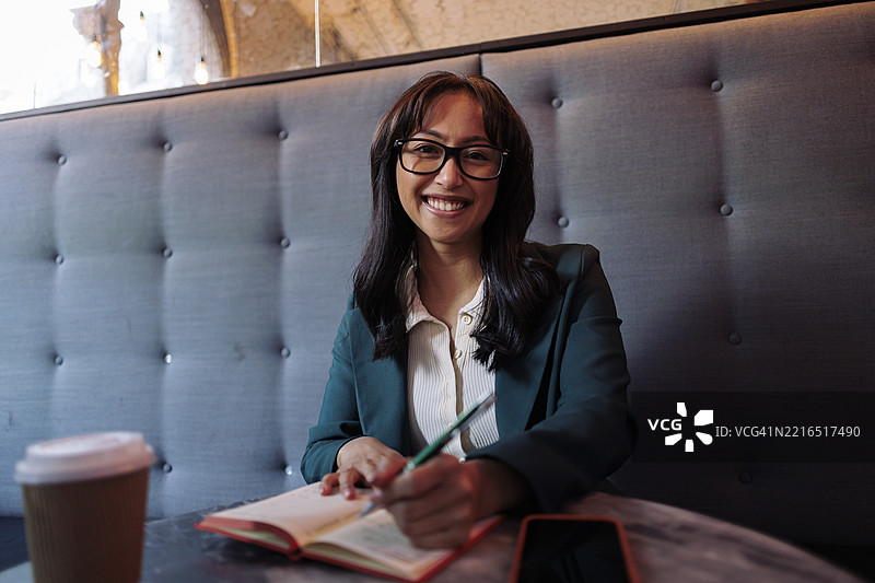微笑着在咖啡馆写笔记的女商人图片素材