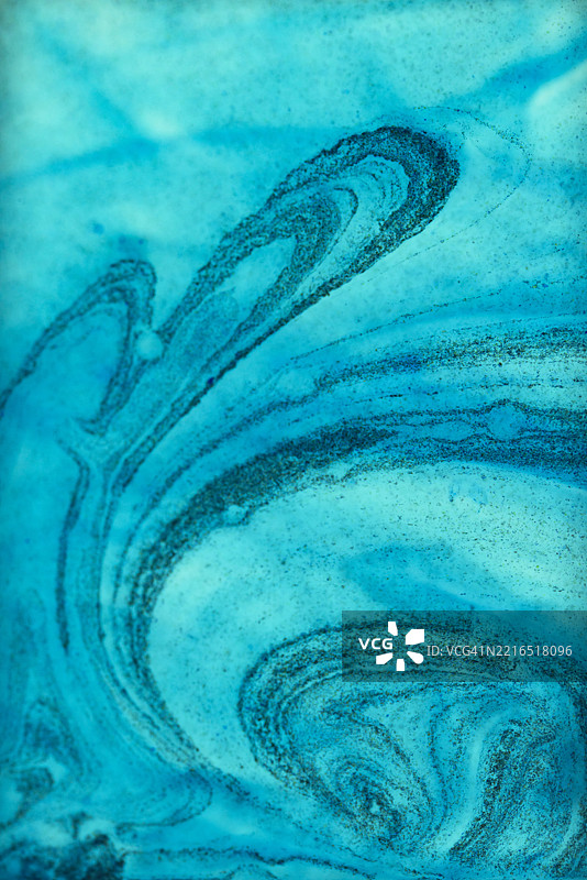 蓝色墨水的漩涡在纸上形成抽象的波浪图案图片素材