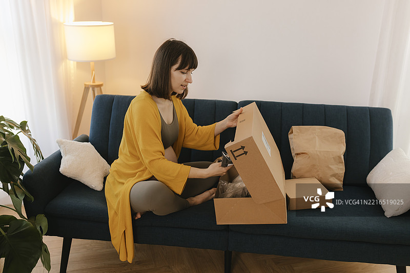 孕妇在舒适的客厅沙发上拆包裹图片素材