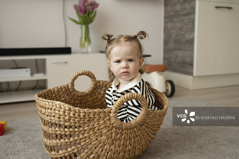 扎着双马尾的小女孩坐在温馨的客厅里的篮子里图片素材
