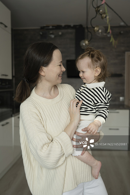母亲在温馨的房间里抱着女儿，彼此微笑。图片素材