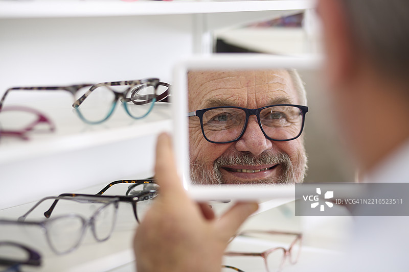 老年男子在商店试戴新眼镜时微笑图片素材