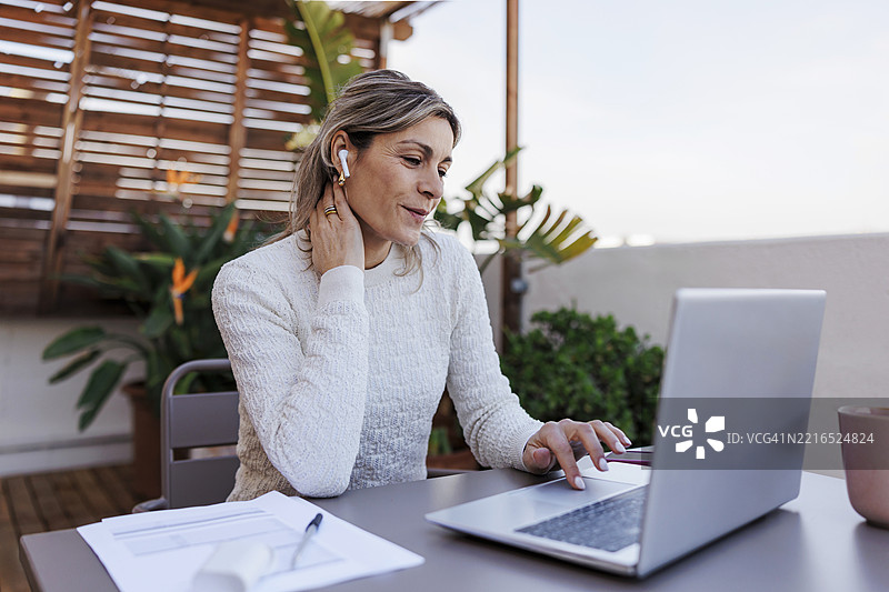 在阳光明媚的屋顶露台上，女商人正在家中使用笔记本电脑工作图片素材