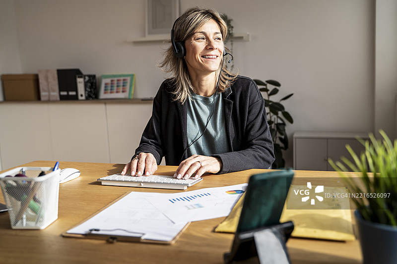在办公室桌子前工作的戴着耳机的女性图片素材