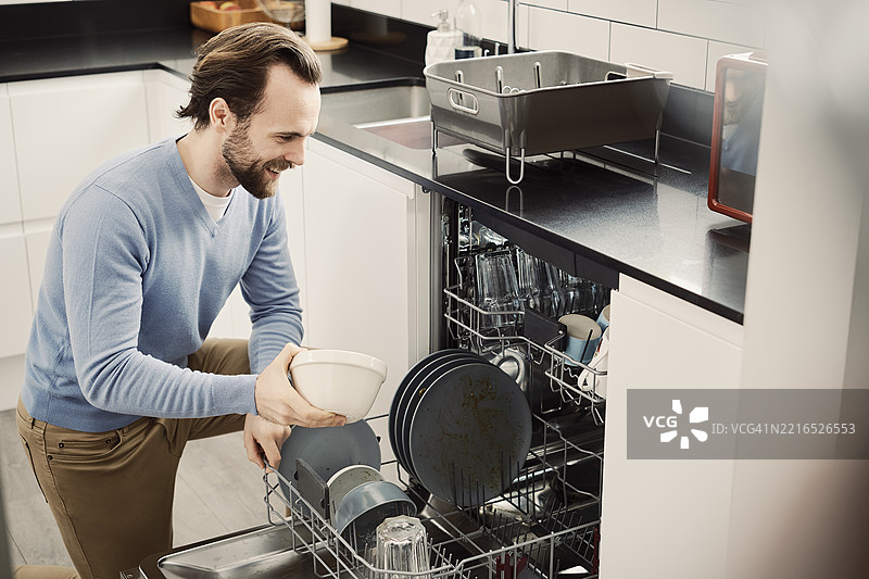 男人在现代厨房里愉快地装载洗碗机图片素材