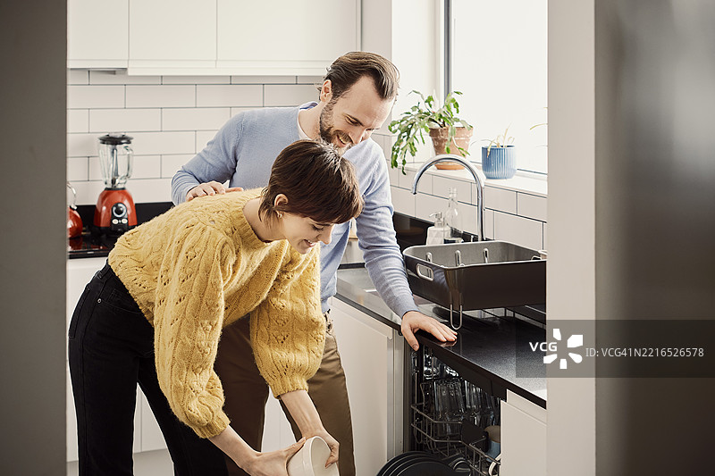 一对情侣在现代厨房里愉快地装载洗碗机图片素材