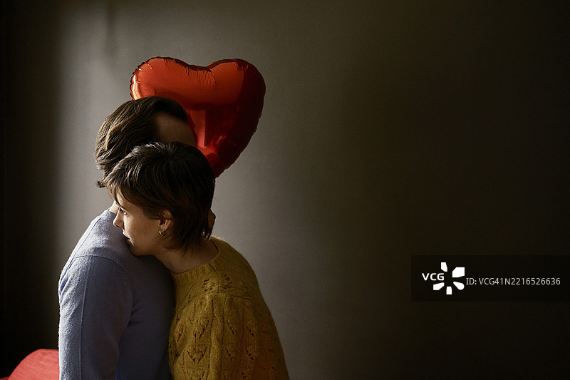 一对情侣在昏暗的房间里拥抱着一个心形气球图片素材