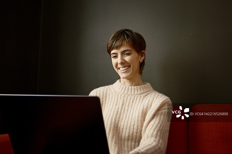 在伦敦的红色沙发上，女性在家中使用笔记本电脑工作图片素材