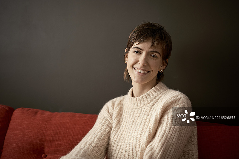 坐在伦敦红色沙发上的女人，面带温暖微笑看向镜头图片素材