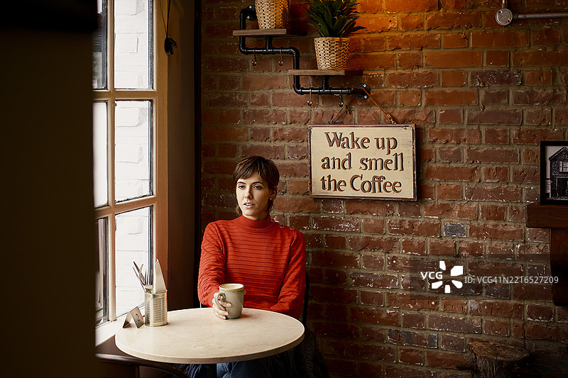 在伦敦咖啡店里，一位女性一边喝咖啡一边望向窗外。图片素材