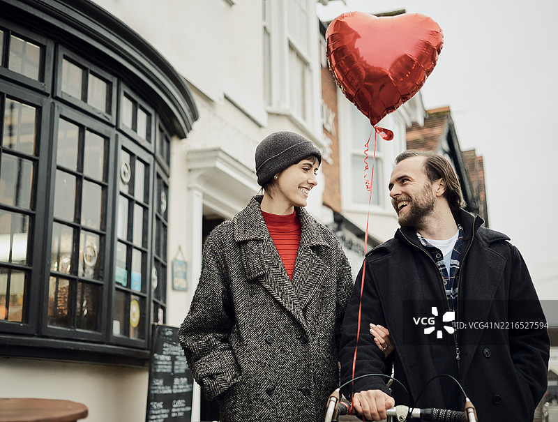 一对情侣在伦敦街头散步，手里拿着心形气球和自行车。图片素材