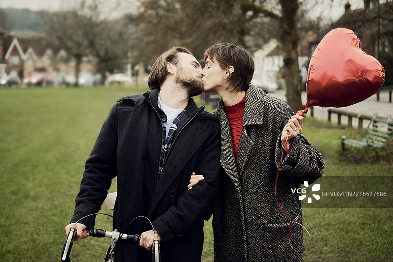 在伦敦公园里亲吻的情侣，手里拿着一个心形气球图片素材