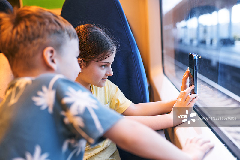 孩子们在火车上一起看智能手机，窗外美丽的风景图片素材