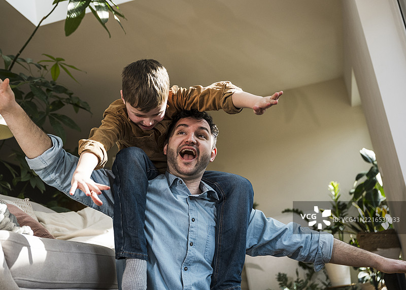 父亲和儿子在室内玩得很开心，儿子坐在父亲的肩膀上。图片素材