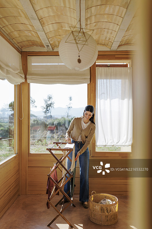 在温馨的阳光房里，女人正在洗衣服，周围是木质内饰。图片素材