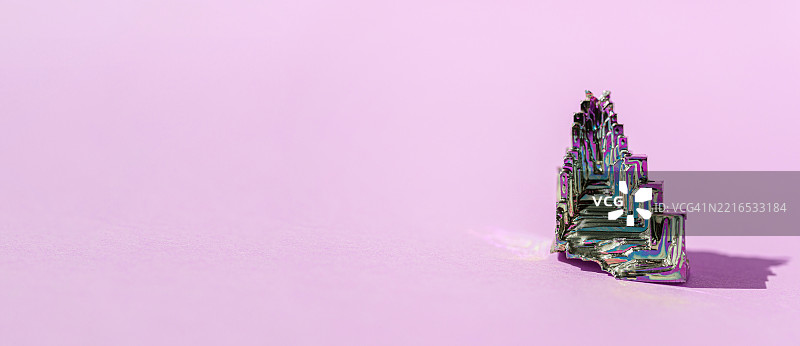 合成铋晶体，表面覆盖有彩虹色氧化膜，背景为粉色图片素材