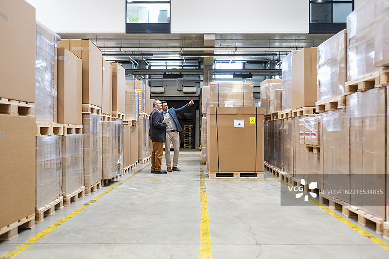 两名员工在仓库中开会，周围是纸箱。图片素材