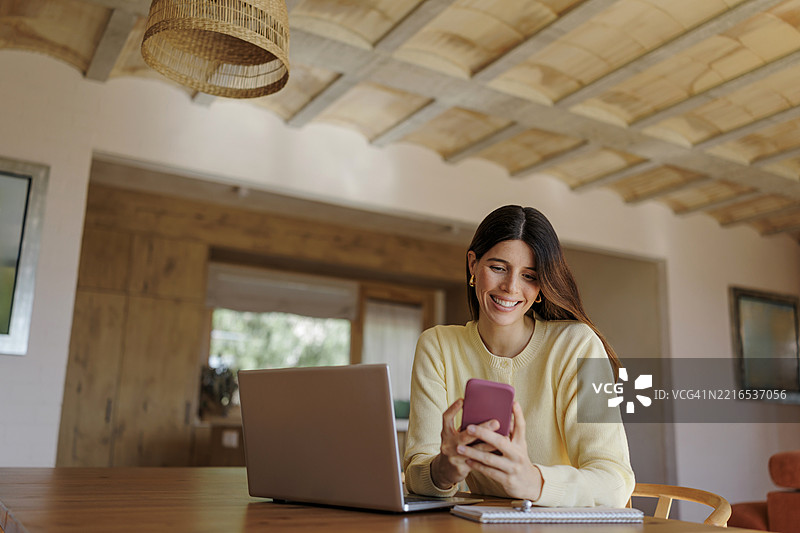 在可持续房屋中，女性使用智能手机和笔记本电脑远程工作图片素材