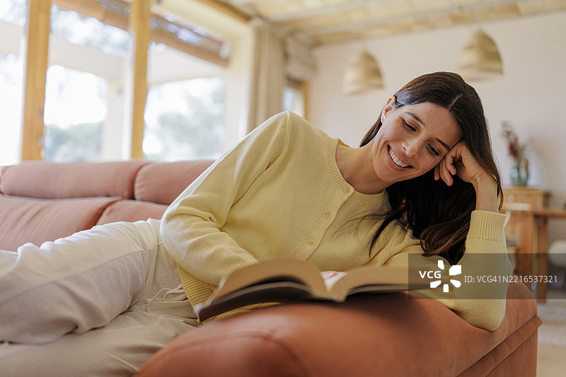 年轻女性在家中沙发上放松，阅读一本书图片素材