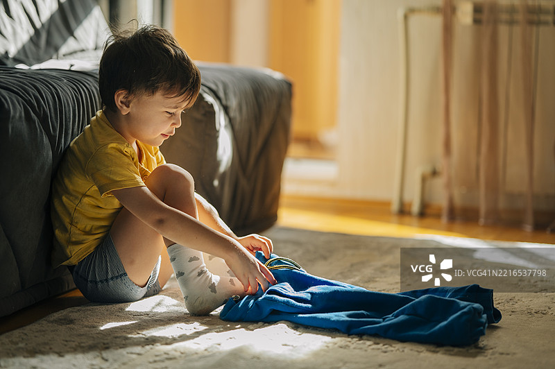 阳光明媚的客厅里，年轻男孩独立穿衣。图片素材