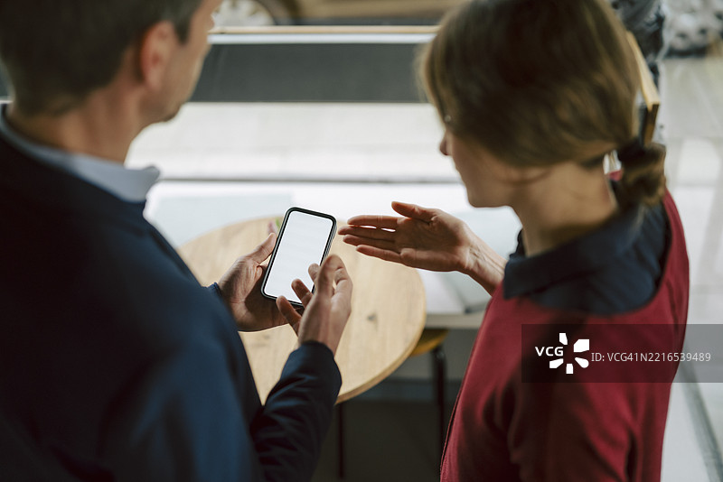 两个人在咖啡馆用智能手机讨论业务图片素材