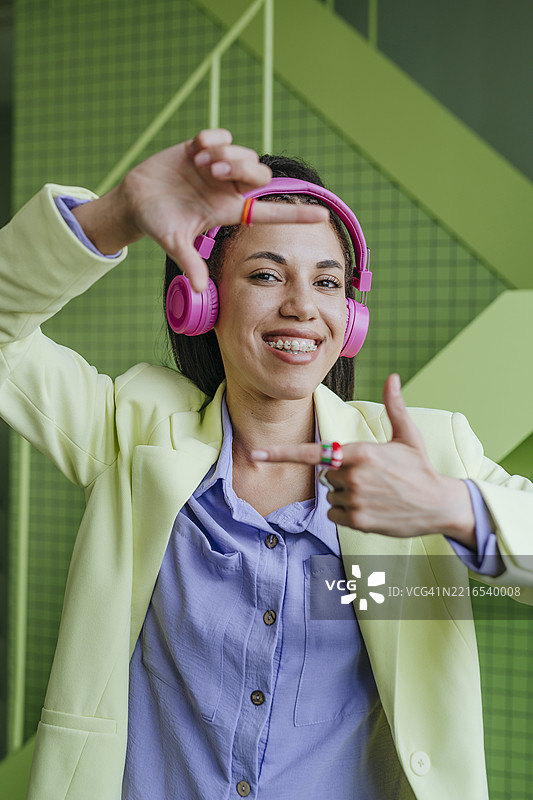 微笑的女性戴着粉色耳机在室内做手势图片素材