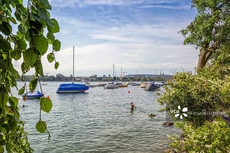 夏季的苏黎世湖，船只和游泳的人们在动态模糊中，背景是瑞士的弗劳明斯特教堂和圣彼得塔。图片素材