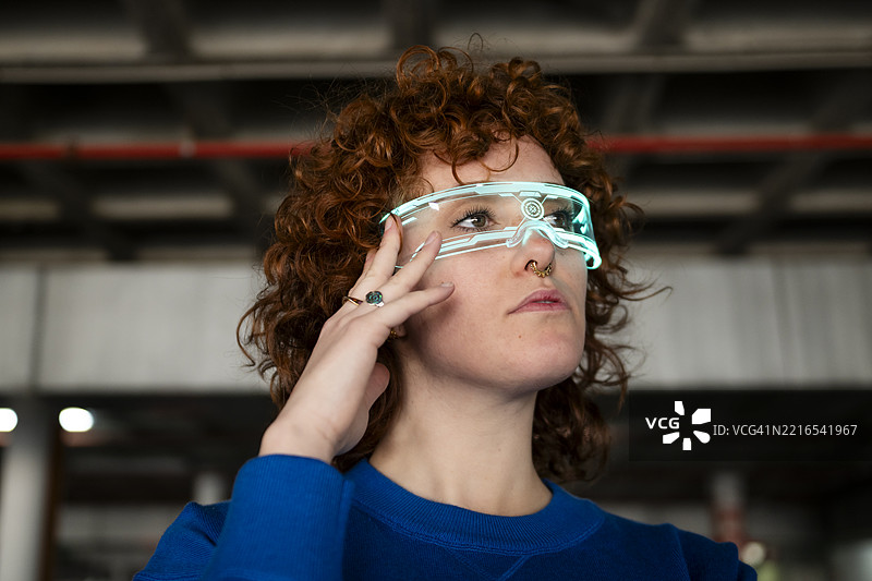 年轻女性在室内佩戴未来感增强现实眼镜，卷发飘逸。图片素材