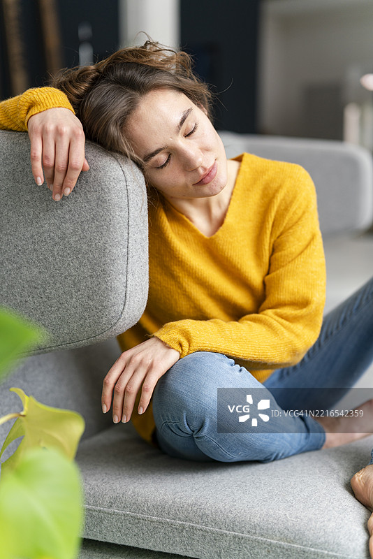 穿着黄色毛衣的女人坐在现代阁楼公寓的沙发上，显得放松而沉思。图片素材
