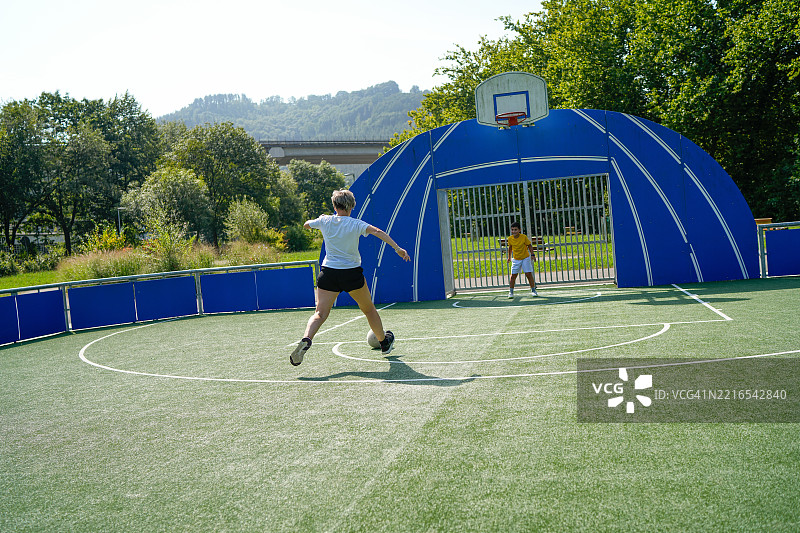 母亲在城市公园里指导儿子踢足球图片素材