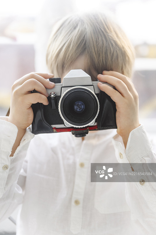 室内一个金发男孩正在使用一台模拟相机图片素材