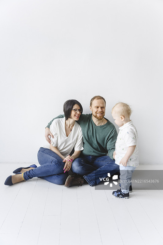 一家人在简约的室内环境中坐在地板上，旁边有一个婴儿。图片素材