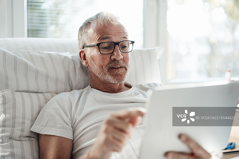 男子在室内床上使用平板电脑获取健康建议图片素材