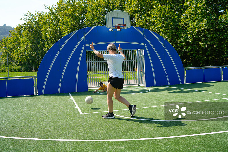 母亲和儿子在城市公园里踢足球和指导彼此图片素材