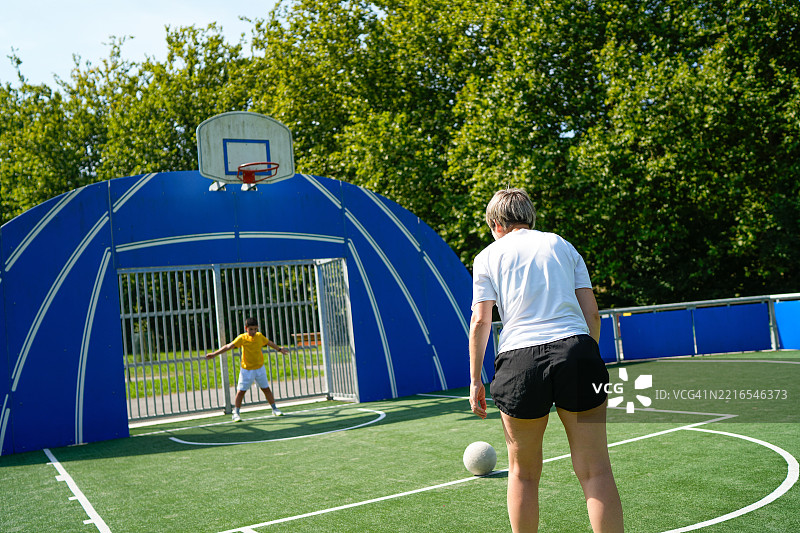 母亲在城市公园里指导儿子踢足球图片素材