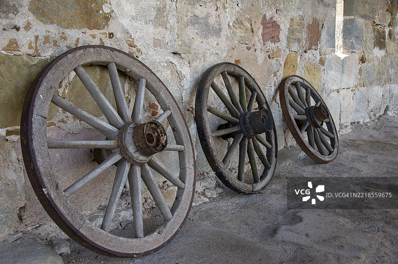 历史悠久的马车轮子靠在一面古老的砂岩墙上图片素材
