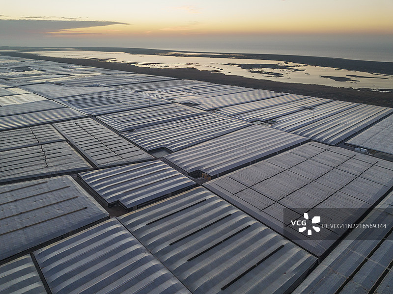 在西班牙安达卢西亚省阿尔梅里亚的埃尔埃希多海岸,晨曦中,盐湖萨利纳斯·德·塞里略斯旁边,成群的闪闪发光的塑料温室,航拍视角。图片素材
