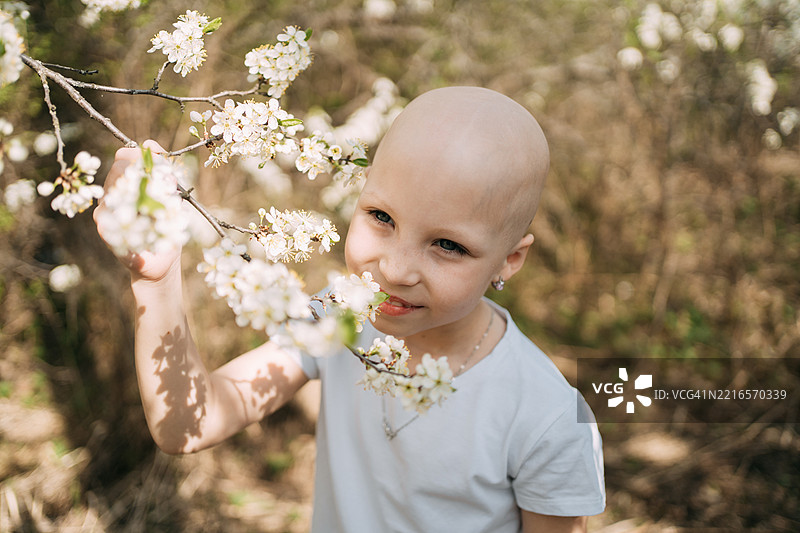 年轻的光头女孩在春天闻樱花的花香图片素材