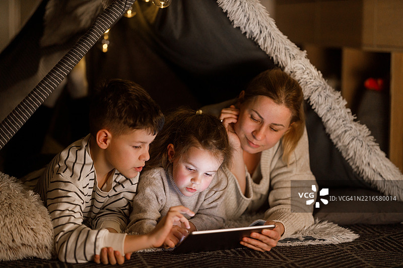 在温馨的毯子堡中，家庭成员们与数字平板一起亲密互动图片素材