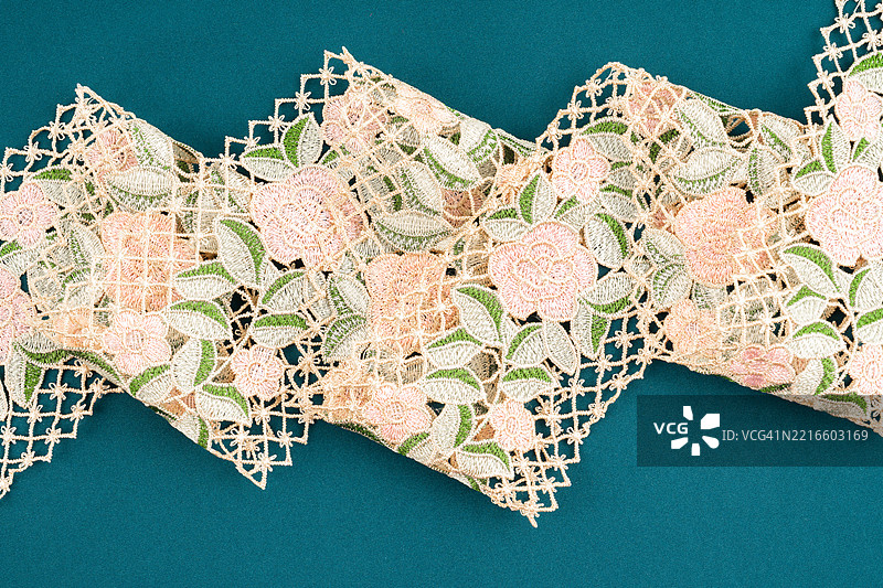 绿色布料背景上的花卉和绿叶蕾丝纺织品图案。图片素材