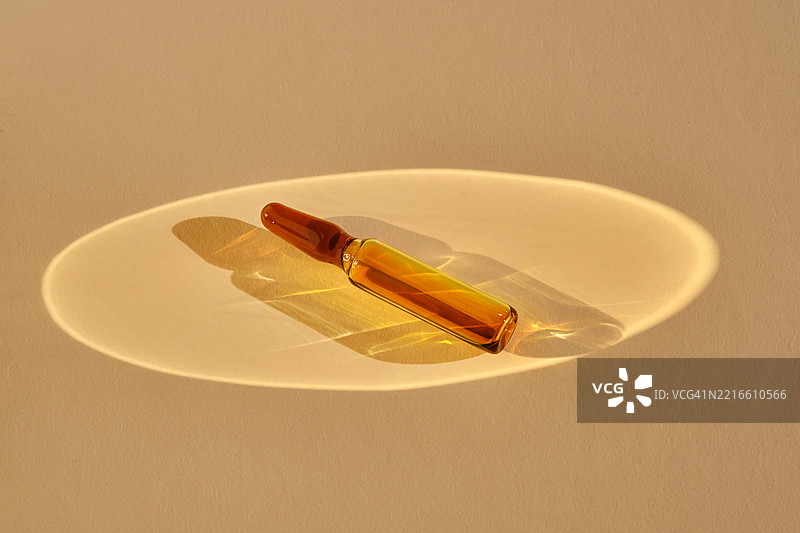 一个装有化妆品或医疗产品的安瓿瓶，背景为米色，散发着美丽的金色光芒。图片素材
