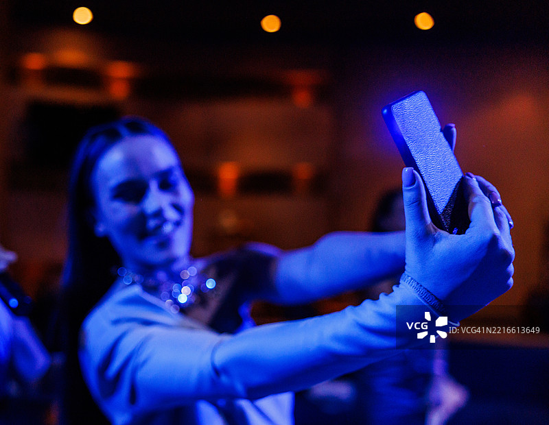年轻女性在夜总会的蓝色霓虹灯下自拍图片素材