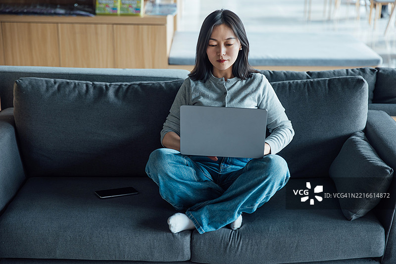 年轻的亚洲女性在办公室大堂坐着使用笔记本电脑图片素材