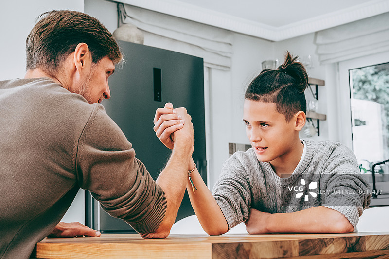 父亲与青少年儿子进行摔跤比赛，家庭共度时光。图片素材