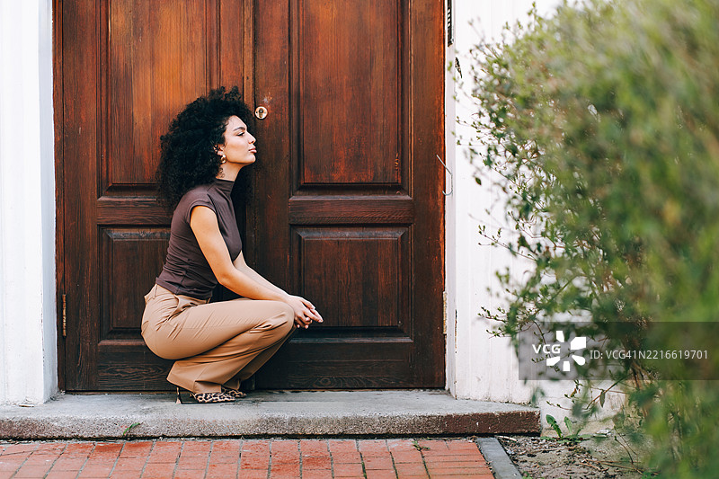 时尚女性蹲在木门旁，展现都市时尚风格图片素材