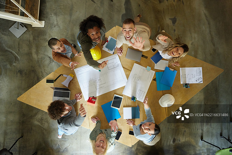 从上方俯瞰快乐的建筑师在办公室中绘制蓝图。图片素材