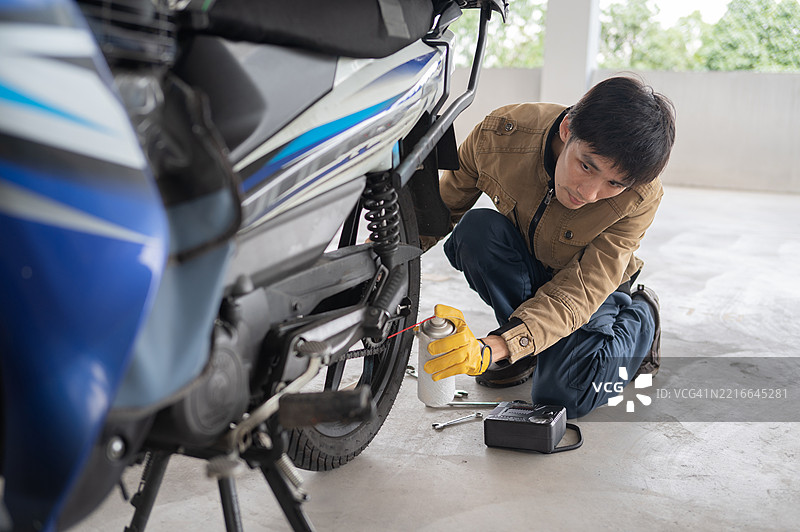 亚洲华裔成年男性在停车场为摩托车进行自我维护，给链条上油的库存照片图片素材
