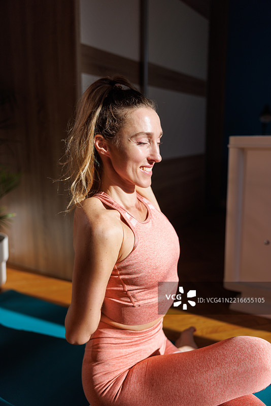 快乐的中年女性坐在垫子上，做着牛面式，正在卧室地板上练习瑜伽图片素材